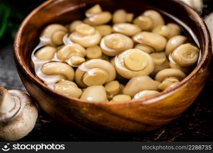 Homemade pickled mushrooms in a wooden bowl. Against a dark background. High quality photo. Homemade pickled mushrooms in a wooden bowl.