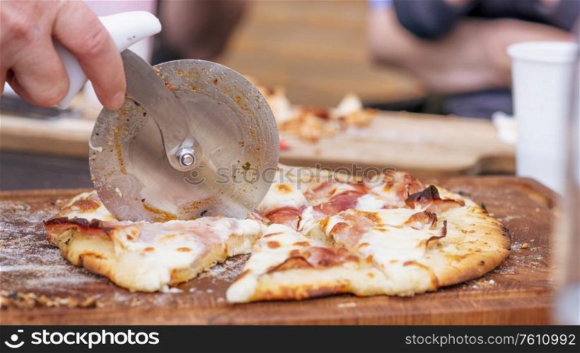 Homemade pizza being sliced on a wooden board in a kitchen