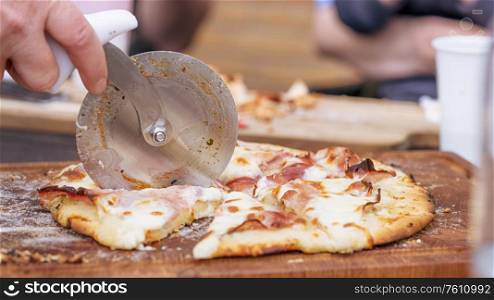 Homemade pizza being sliced on a wooden board in a kitchen