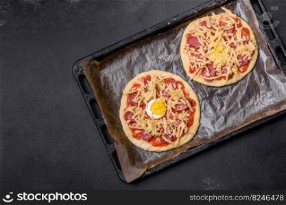 Homemade pizza with sausages, tomatoes, cheese, spices and herbs on a wooden cutting board against a dark concrete background. Homemade pizza with sausages, tomatoes, cheese, spices and herbs on a wooden cutting board
