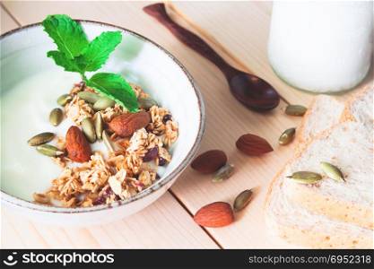 Homemade plain yogurt with almond granola and pumpkin seeds. Fresh milk and whole wheat breads on wooden table