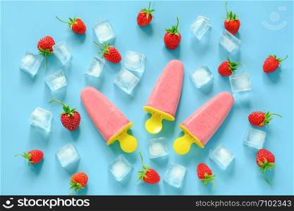 Homemade popsicles. Natural ice cream in bright plastic molds, strawberries and ice cubes on blue background. Top view Flat lay.. Homemade popsicles. Natural ice cream in bright plastic molds, strawberries and ice cubes on blue background. Top view Flat lay