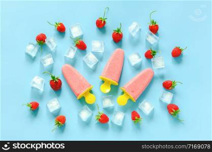 Homemade popsicles. Natural ice cream in bright plastic molds, strawberries and ice cubes on blue background. Top view Flat lay.. Homemade popsicles. Natural ice cream in bright plastic molds, strawberries and ice cubes on blue background. Top view Flat lay