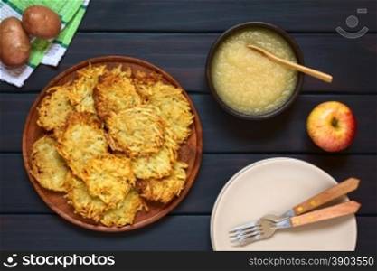 Homemade potato pancakes or fritters on wooden plate with apple sauce, a traditional dish in Germany, photographed overhead on dark wood with natural light