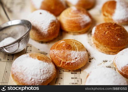 Homemade profiteroles on the music sheet with notes. Profiteroles  choux a la creme  - French choux pastry balls filled with custard or cottage cheese sprinkled with powdered sugar