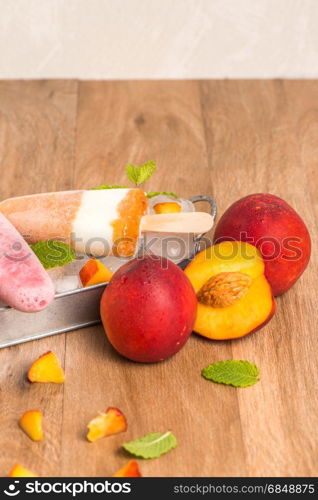 Homemade raspberries and peach popsicles on a wooden table.