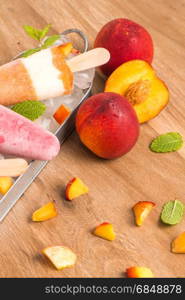 Homemade raspberries and peach popsicles on a wooden table.