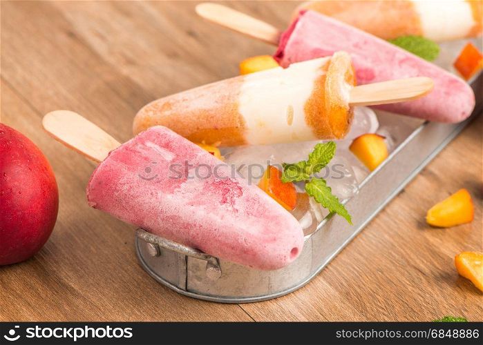Homemade raspberries and peach popsicles on a wooden table.