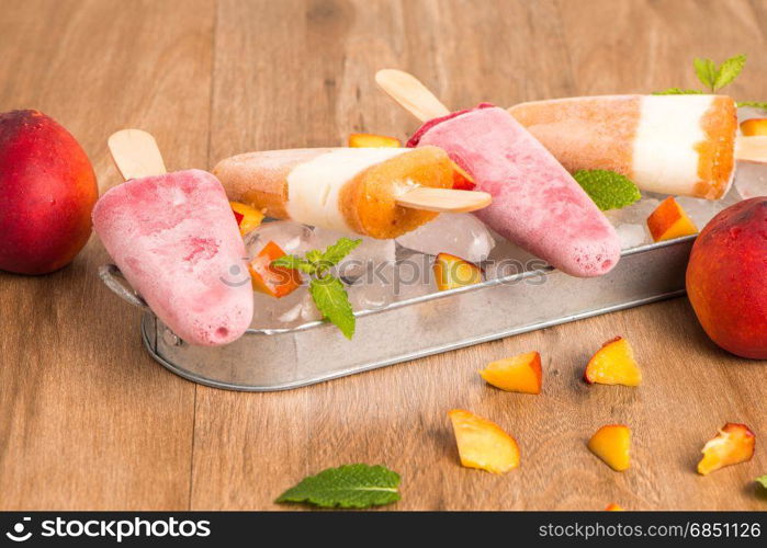 Homemade raspberries and peach popsicles on a wooden table.