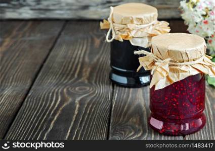 Homemade raspberry and blueberry jam in glass jars on a wooden table. Close-up with copy space for text, selective focus