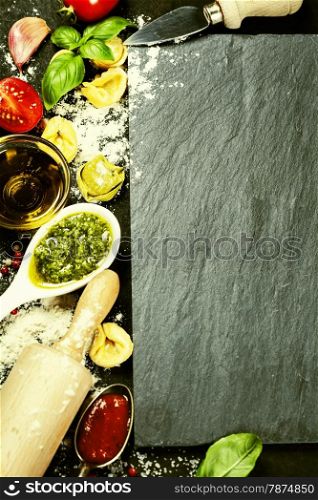 Homemade raw Italian tortellini and basil leaves and pesto on dark vintage background