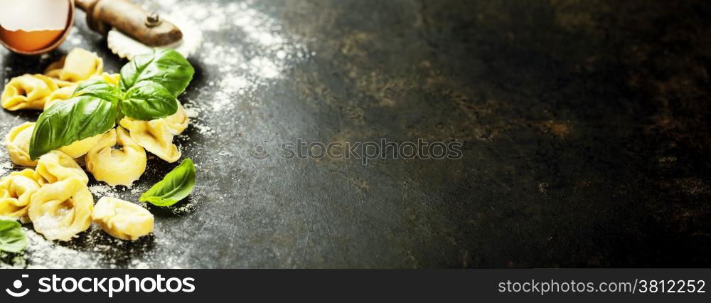 Homemade raw Italian tortellini and basil leaves on dark vintage background