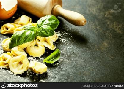 Homemade raw Italian tortellini and basil leaves on dark vintage background