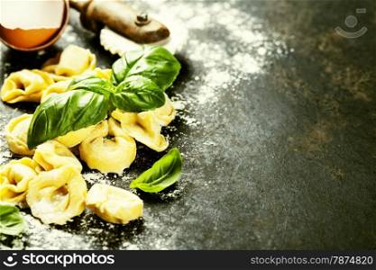 Homemade raw Italian tortellini and basil leaves on dark vintage background