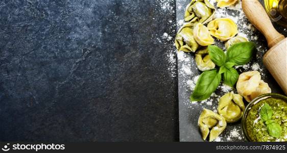 Homemade raw Italian tortellini, basil leaves and pesto on dark vintage background