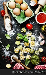 Homemade raw Italian tortellini, basil leaves,flour, tomatoes and basil on dark vintage background