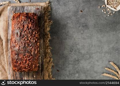 Homemade rectangular wheat and rye bread with seeds, top view. Freshly baked naturally fermented bread lies on a wooden board, a gray table with space for text