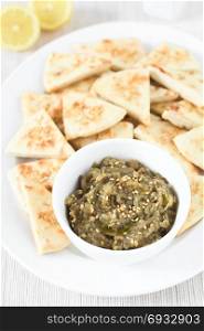 Homemade roasted eggplant dip or spread, baba ganoush in the Mediterranean cuisine, with olive oil and sesame on top, homemade sesame pita chips on the side, photographed with natural light (Selective Focus, Focus in the middle of the dip). Roasted Eggplant Dip or Spread with Pita Chips