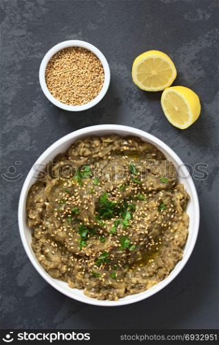 Homemade roasted eggplant dip or spread, baba ganoush in the Mediterranean cuisine, with olive oil, sesame and parsley on top, photographed overhead on slate with natural light. Roasted Eggplant Dip or Spread