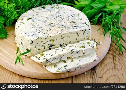 Homemade round cheese with herbs and spices, cut into slices on a wooden boards background