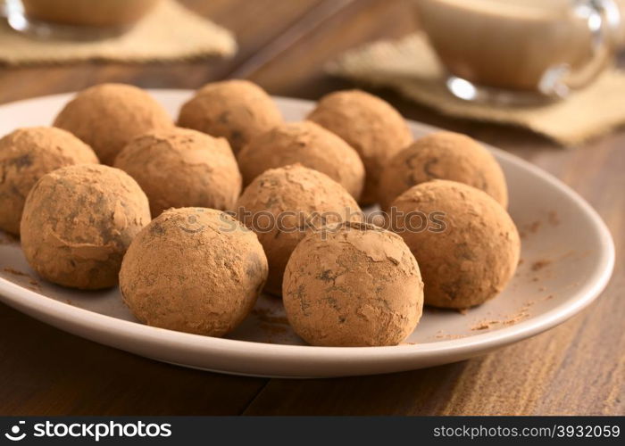 Homemade rum balls covered with cocoa powder, glass cups of hot chocolate in the back, photographed with natural light (Selective Focus, Focus on the two balls in the front)