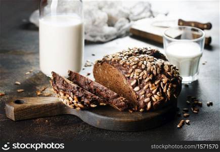 Homemade rustic rye bread with sunflower seeds and a bottle of milk on old table