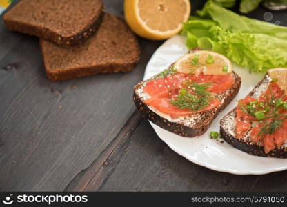 Homemade sandwich with salmon and rye bread , butter lemon, and lettuce for breakfast