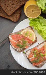 Homemade sandwich with salmon and rye bread , butter lemon, and lettuce for breakfast