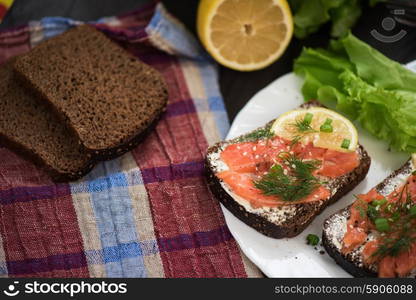 Homemade sandwich with salmon and rye bread , butter lemon, and lettuce for breakfast