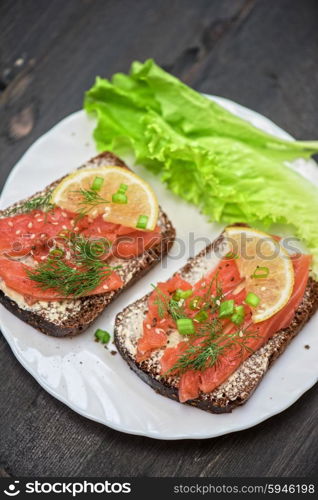 Homemade sandwich with salmon and rye bread , butter lemon, and lettuce for breakfast