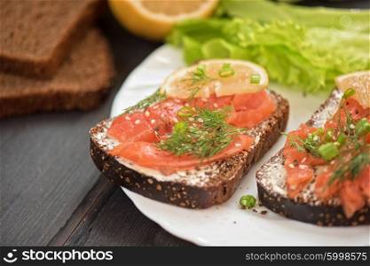 Homemade sandwich with salmon and rye bread , butter lemon, and lettuce for breakfast