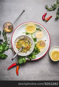 Homemade sauce or salad dressing in bowl with ingredients: fresh herbs, oil, lemon and honey on gray concrete background, top view, flat lay. Healthy , clean food concept