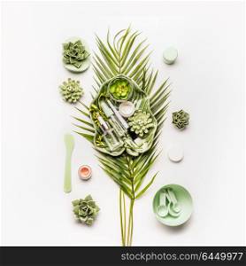 Homemade skin care setting . Herbal cosmetic mask making. Tropical leaves and succulents with cosmetic products and accessories: Mask Brush, bowl, spatula, measuring spoons on white desktop background