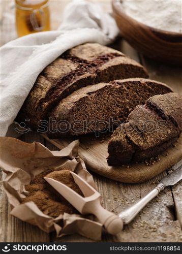 Homemade sliced round rye bread on a wooden table with malt and flour