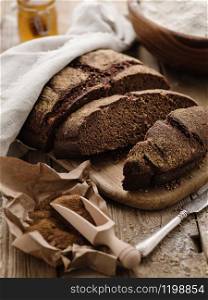 Homemade sliced round rye bread on a wooden table with malt and flour