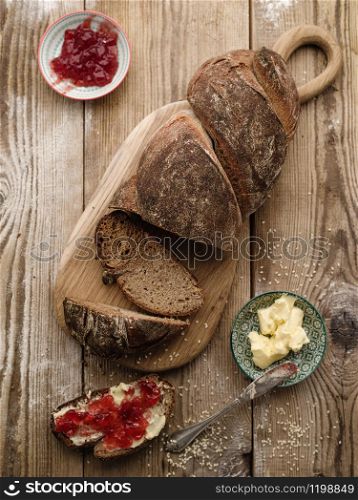 Homemade sliced rye bread on a wooden table and a sandwich with butter and jam