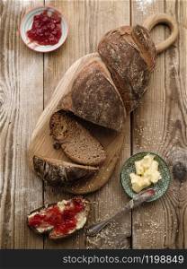 Homemade sliced rye bread on a wooden table and a sandwich with butter and jam