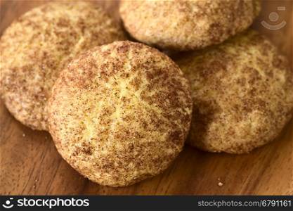 Homemade snickerdoodle cookies with cinnamon and sugar coating on wooden plate, photographed with natural light (Selective Focus, Focus in the middle of the cookie in the front)