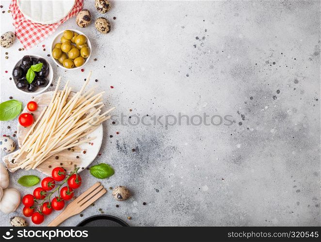 Homemade spaghetti pasta with quail eggs with bottle of tomato sauce and cheese on stone background. Classic italian village food. Garlic, champignons, black and green olives, pan and spatula