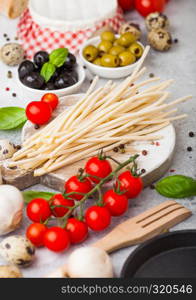 Homemade spaghetti pasta with quail eggs with bottle of tomato sauce and cheese on stone background. Classic italian village food. Garlic, champignons, black and green olives, pan and spatula