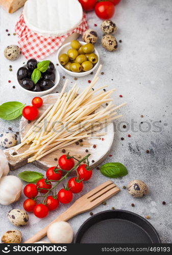 Homemade spaghetti pasta with quail eggs with bottle of tomato sauce and cheese on stone background. Classic italian village food. Garlic, champignons, black and green olives, pan and spatula