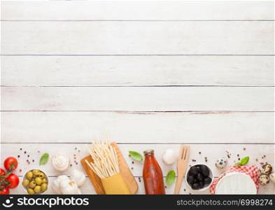 Homemade spaghetti pasta with quail eggs with bottle of tomato sauce and cheese on wood background. Classic italian village food. Garlic, champignons, black and green olives, oil and spatula
