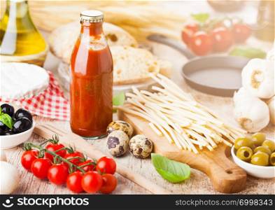 Homemade spaghetti pasta with quail eggs with bottle of tomato sauce and cheese on wooden background. Classic italian village food. Garlic, black and green olives, oil and bread.