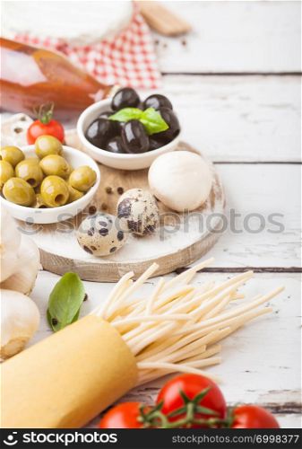 Homemade spaghetti pasta with quail eggs with bottle of tomato sauce and cheese on wood background. Classic italian village food. Garlic, champignons, black and green olives