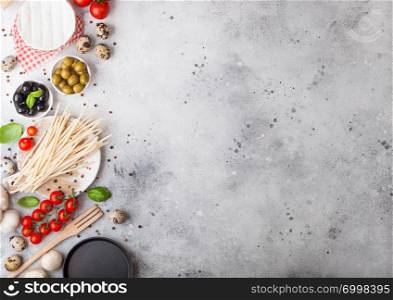 Homemade spaghetti pasta with quail eggs with bottle of tomato sauce and cheese on stone background. Classic italian village food. Garlic, champignons, black and green olives, pan and spatula
