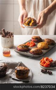 Homemade spicy pumpkin muffins or cupcakes with chocolate on a metal rack with woman hands in the background. Autumn dessert. Selective focus. spicy pumpkin muffins