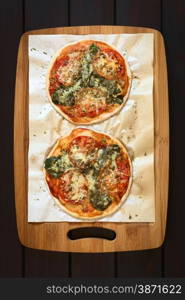 Homemade spinach and tomato pizza on baking paper on wooden board, photographed overhead on dark wood with natural light