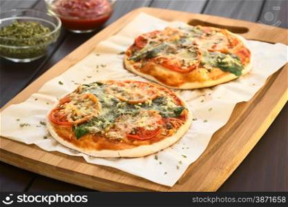 Homemade spinach and tomato pizza on baking paper on wooden board, photographed on dark wood with natural light (Selective Focus, Focus one third into the first pizza)