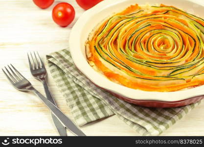 Homemade spiral vegetable tart pie of carrots, zucchini and eggplant with bechamel sauce on white wooden background. Rustic style, selective focus, close up, copy space for text. Italian cuisine. Homemade spiral vegetable tart pie of carrots, zucchini and eggplant on white wooden background