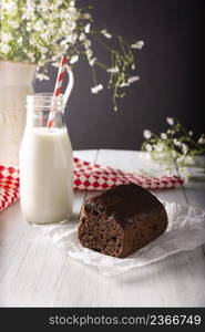 Homemade sponge chocolate cake with chocolate glaze and glass of milk on white rustic wooden surface